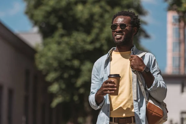 Позитивний, стильний афроамериканський чоловік тримає каву, щоб піти і подивитися — стокове фото