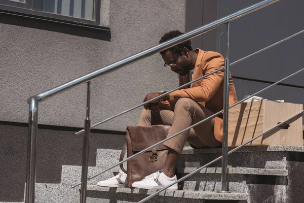 Aufgebrachter, entlassener afrikanisch-amerikanischer Geschäftsmann sitzt auf Treppe neben Pappschachtel — Stockfoto