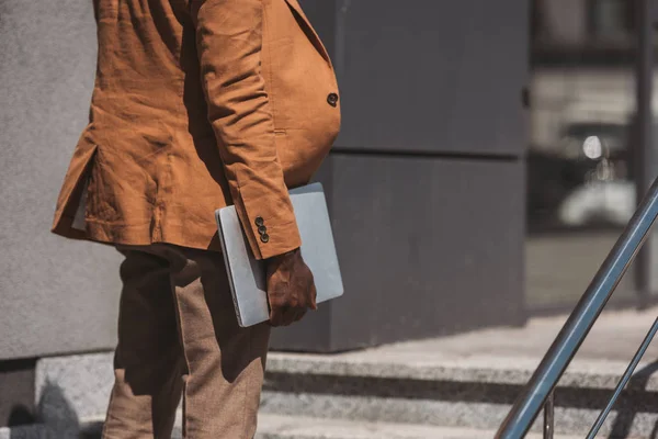 Ausgeschnittene Ansicht eines afrikanisch-amerikanischen Geschäftsmannes mit Laptop während er auf einer Treppe steht — Stockfoto