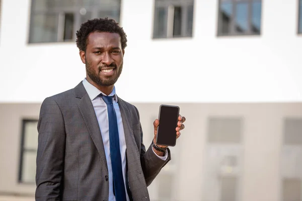 Alegre afroamericano empresario mostrando teléfono inteligente con pantalla en blanco y sonriendo a la cámara - foto de stock