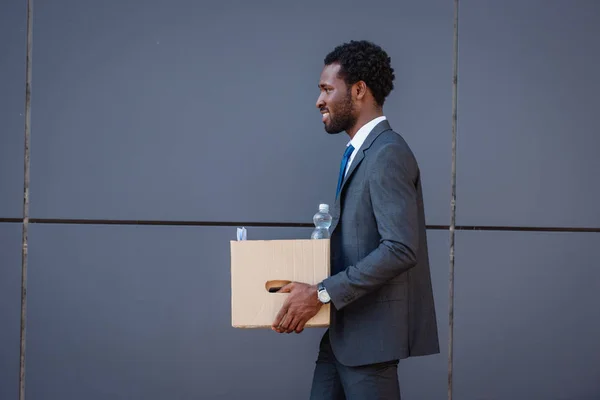 Вид збоку красивий афроамериканський бізнесмен тримає картонну коробку — стокове фото