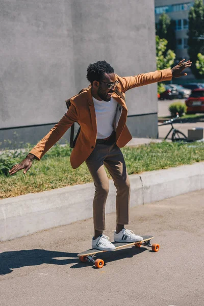 Joyeux homme d'affaires afro-américain chevauchant longboard sur la rue ensoleillée — Photo de stock