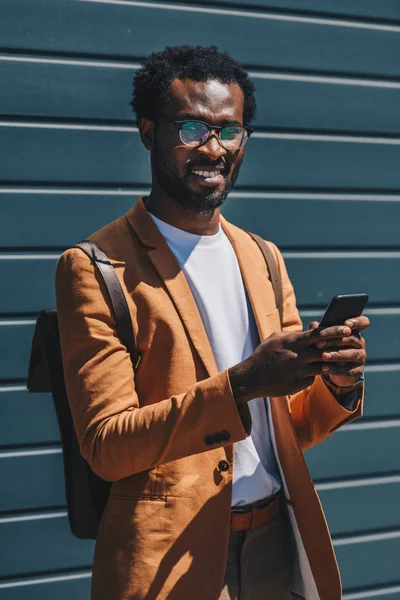 Empresário afro-americano positivo olhando para a câmera enquanto usa o smartphone — Fotografia de Stock