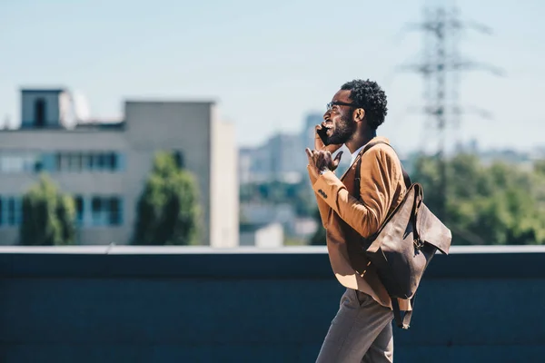 Stylischer afrikanisch-amerikanischer Geschäftsmann spricht auf dem Smartphone während er auf dem Dach spaziert — Stockfoto