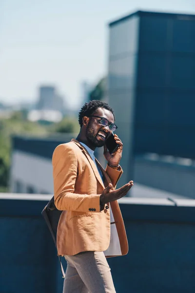 Emocionado hombre de negocios afroamericano hablando en el teléfono inteligente y el gesto en la azotea - foto de stock