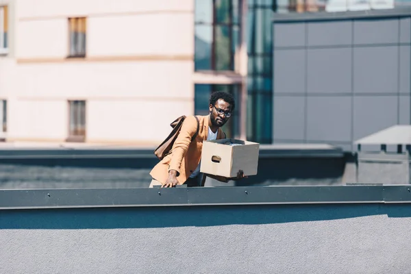 Sconvolto uomo d'affari guardando giù dal tetto mentre teneva scatola di cartone — Foto stock