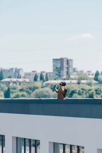 Афроамериканський чоловік жестикулює з піднятими руками, стоячи на даху — стокове фото