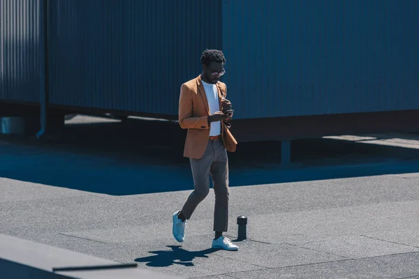 Hombre de negocios afroamericano elegante usando el ordenador portátil mientras que camina en la azotea - foto de stock