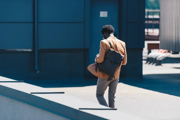 Vista trasera del elegante hombre de negocios afroamericano con bolsa caminando en la azotea - foto de stock