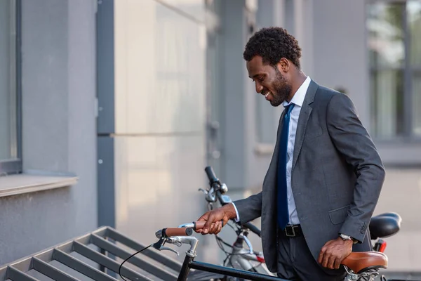 Homme d'affaires afro-américain positif souriant tout en prenant le vélo du parking — Photo de stock