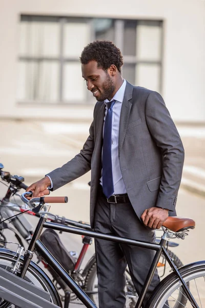 Alegre empresário afro-americano sorrindo enquanto toma bicicleta do estacionamento — Fotografia de Stock