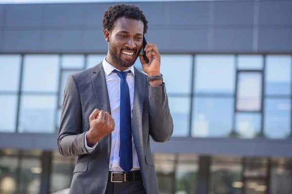 Happy african american businessman showing yes gesture while talking on smartphone — Stock Photo