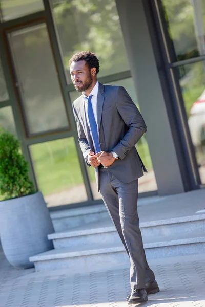 Apuesto hombre de negocios afroamericano mirando hacia otro lado mientras está de pie cerca del edificio de oficinas - foto de stock