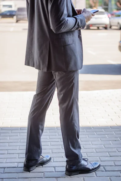 Vista recortada del hombre de negocios afroamericano utilizando el teléfono inteligente en la calle - foto de stock