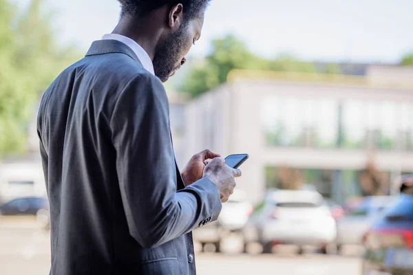 Serio uomo d'affari afroamericano in giacca e cravatta utilizzando smartphone su strada — Foto stock