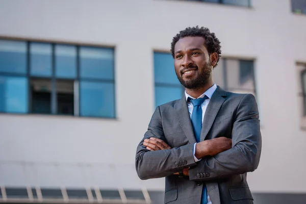 Веселий афроамериканець бізнесмен посміхається, стоячи з перехрещеними обіймами — стокове фото