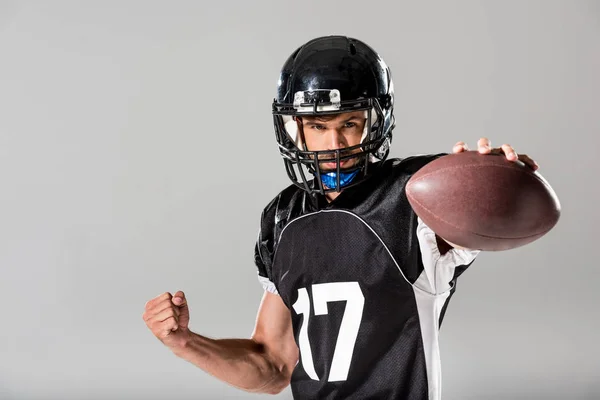 Американский футболист в шлеме с мячом, изолированным от серого — стоковое фото