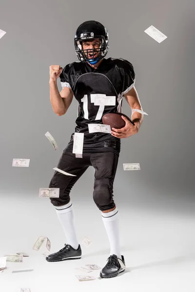 Aufgeregter American Football-Spieler mit Ball auf grau mit fallendem Geld — Stockfoto