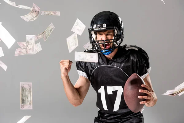 Emocionado jugador de fútbol americano con pelota en gris con la caída de dinero - foto de stock