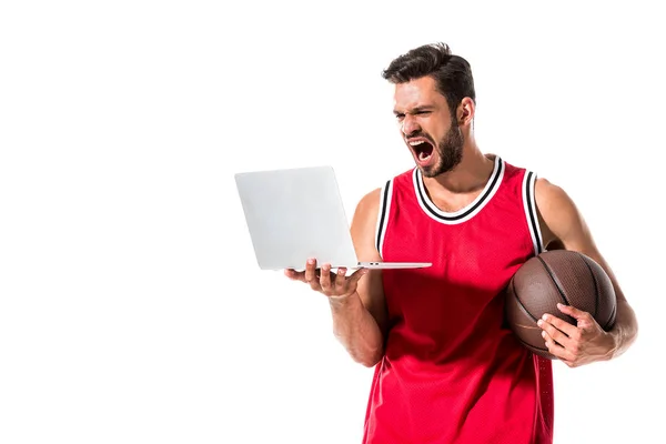 Jugador de baloncesto gritando con la bola usando el ordenador portátil aislado en blanco - foto de stock