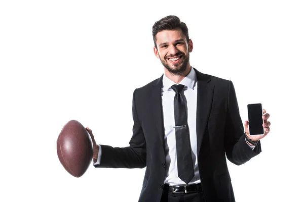 Hombre de negocios feliz en ropa formal con pelota de rugby y teléfono inteligente aislado en blanco - foto de stock
