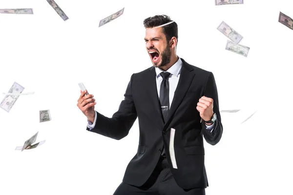 Excitado hombre de negocios con teléfono inteligente cerca de la caída de billetes de dólar Aislado en blanco - foto de stock