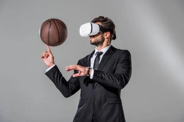 Businessman in Virtual reality headset spinning on finger basketball on grey — Stock Photo