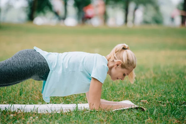 Mulher madura atraente fazendo exercício prancha enquanto racticing ioga no gramado verde no parque — Fotografia de Stock