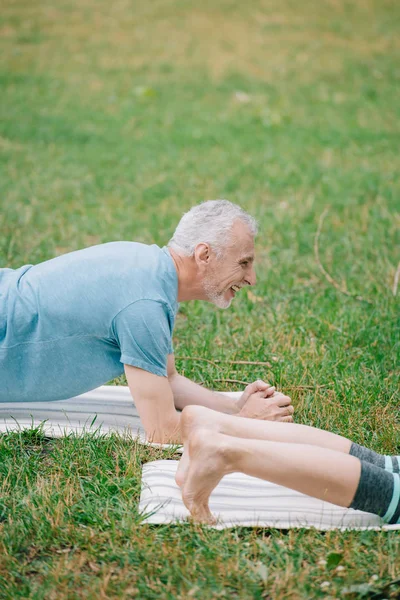 Vista ritagliata della donna e sorridente uomo maturo facendo esercizio tavola durante la pratica dello yoga nel parco — Foto stock