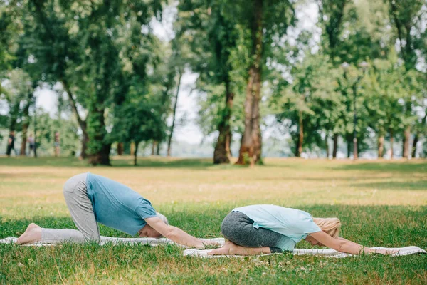 Mature man and woman practicing relaxation yoga poses on yoga mats on lawn — Stock Photo