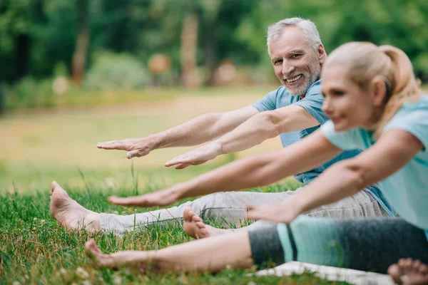 Селективный фокус зрелого мужчины и женщины на ковриках для йоги, практикующих йогу в парке — стоковое фото
