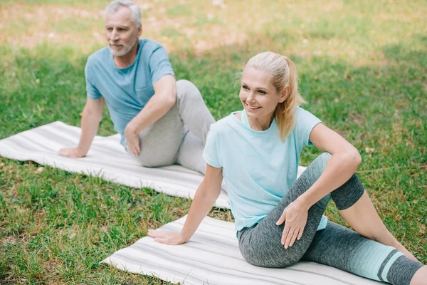 Mature homme et femme souriant tout en pratiquant le yoga dans le parc — Photo de stock