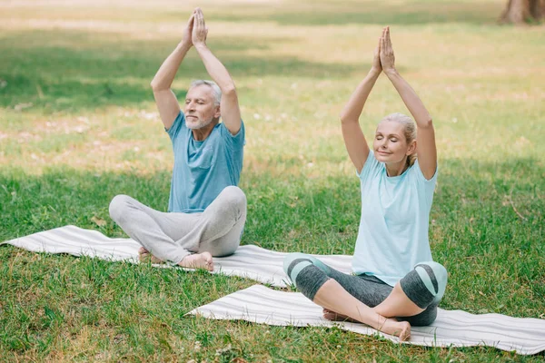 Mature man and woman sitting in lotus poses and meditating in park — Stock Photo