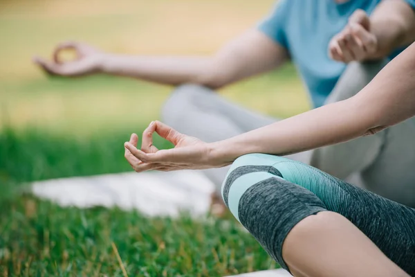 Visão parcial do homem e da mulher meditando em poses de ioga enquanto sentado no gramado verde — Fotografia de Stock