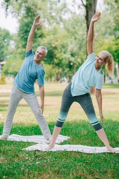 Hombre y mujer maduros practicando yoga guerrero posa mientras están de pie en colchonetas de yoga - foto de stock