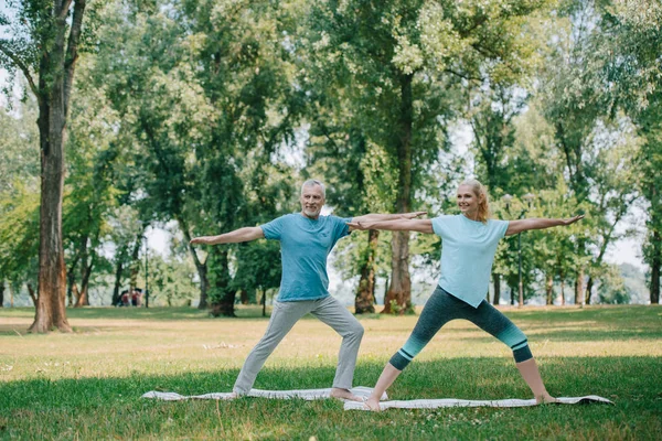 Sonriente hombre y mujer de pie en yoga posa mientras practica yoga en el parque - foto de stock