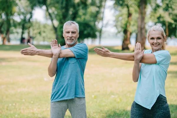 Souriant mature homme et femme exerçant dans le parc ensemble et souriant à la caméra — Photo de stock