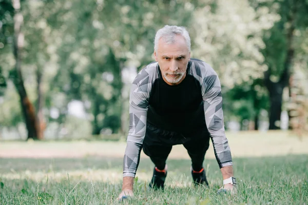 Handsome mature sportsman in sportswear doing push ups on lawn in park — Stock Photo