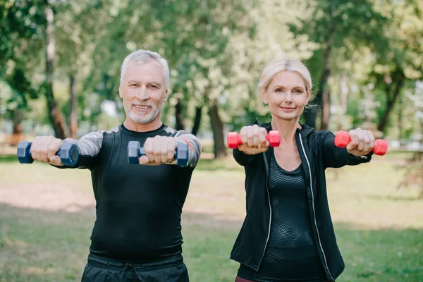 Sportif mature souriant et sportive faisant des exercices avec des cloches et souriant à la caméra — Photo de stock