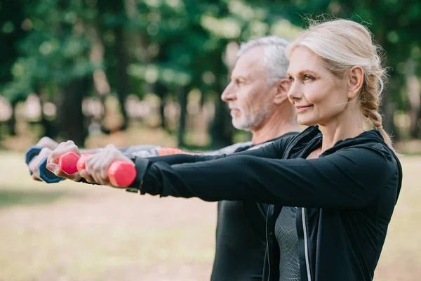 Selective focus of smiling sportswoman training with barbells together with mature sportsman — Stock Photo