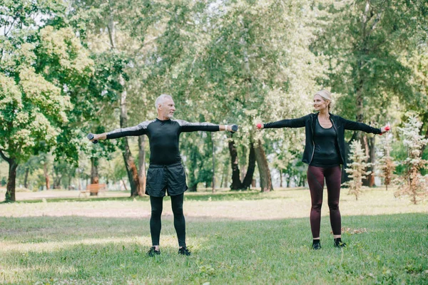 Взрослый спортсмен и спортсменка смотрят друг на друга во время тренировки с штангой в парке — стоковое фото
