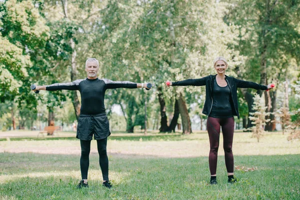 Mature sportsman and sportswoman looking at camera while training with barbells in park — Stock Photo