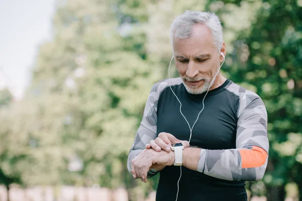 Beau sportif mature regardant fitness suivi tout en écoutant de la musique dans les écouteurs — Photo de stock