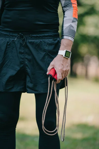 Cropped view of mature sportsman in fitness tracker holding jump rope — Stock Photo