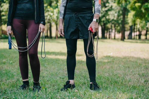 Cropped view of mature sportsman and sportswoman holding jump ropes — Stock Photo