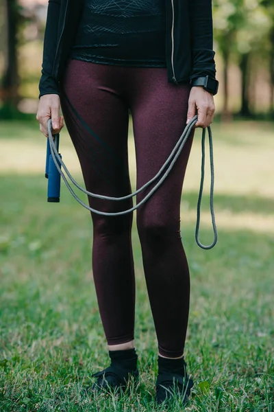 Cropped view of mature sportswoman standing in park and holding jump rope — Stock Photo