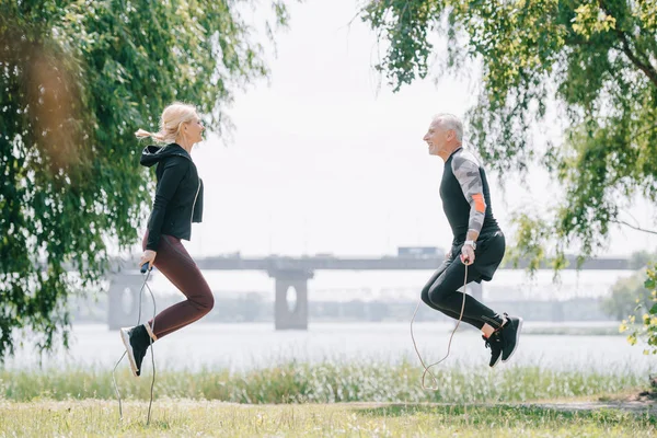 Vista lateral de deportista maduro y entrenamiento de deportista con cuerdas de salto en el parque juntos - foto de stock