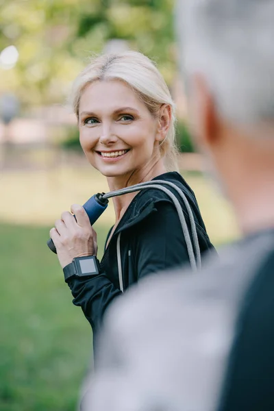 Selective focus of smiling sportsman with jump rope looking at mature sportsman — Stock Photo