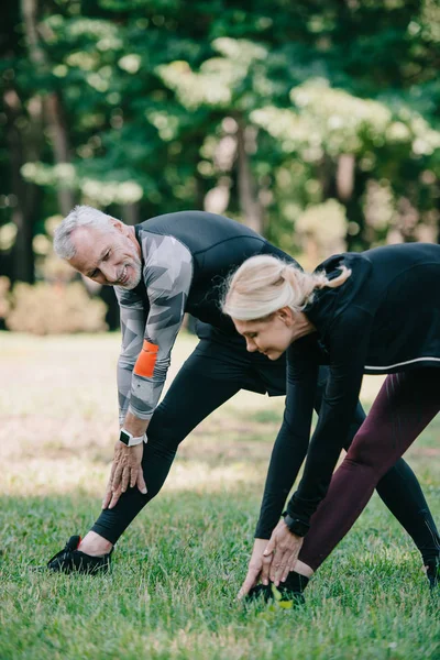 Smiling, mature sportsman and sportswoman warming up in park together — Stock Photo