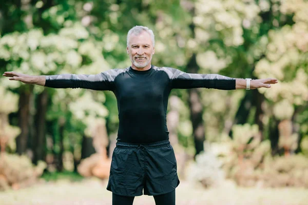 Cheerful, mature sportsman smiling at camera while training in park — Stock Photo